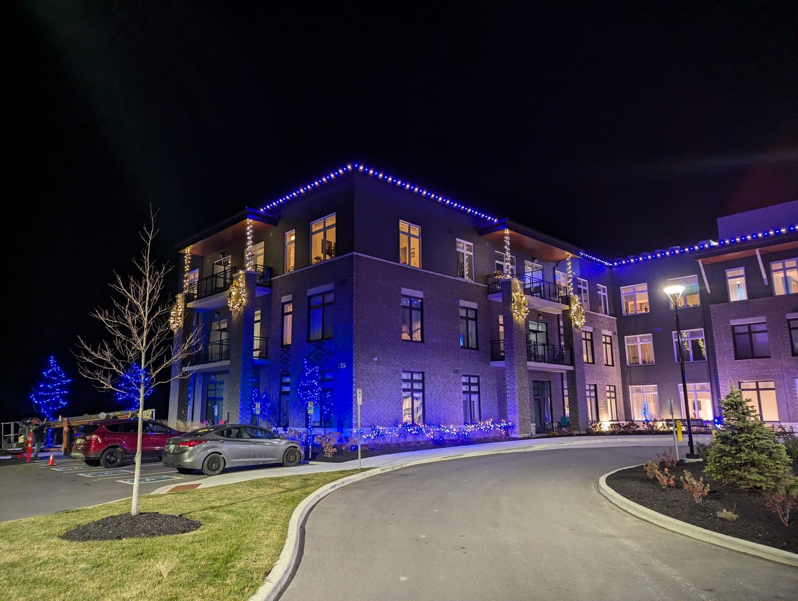 Multi-storey commercial building with blue roofline lights and warm-white column garland at night