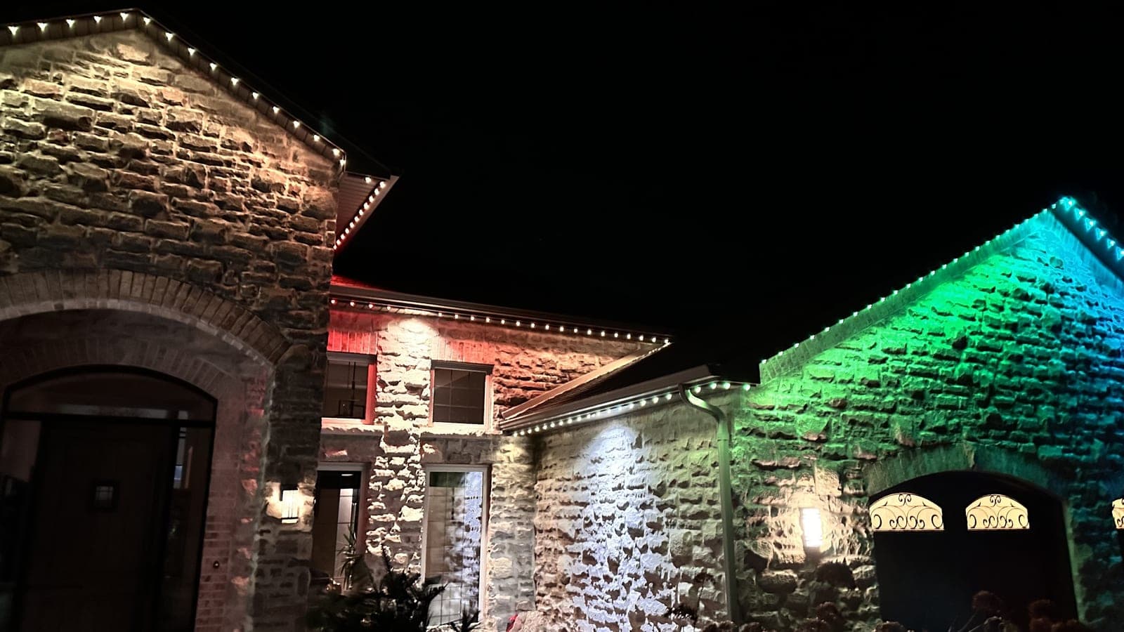 Stone home with colour-changing red, green and blue roofline lights and facade uplighting at night