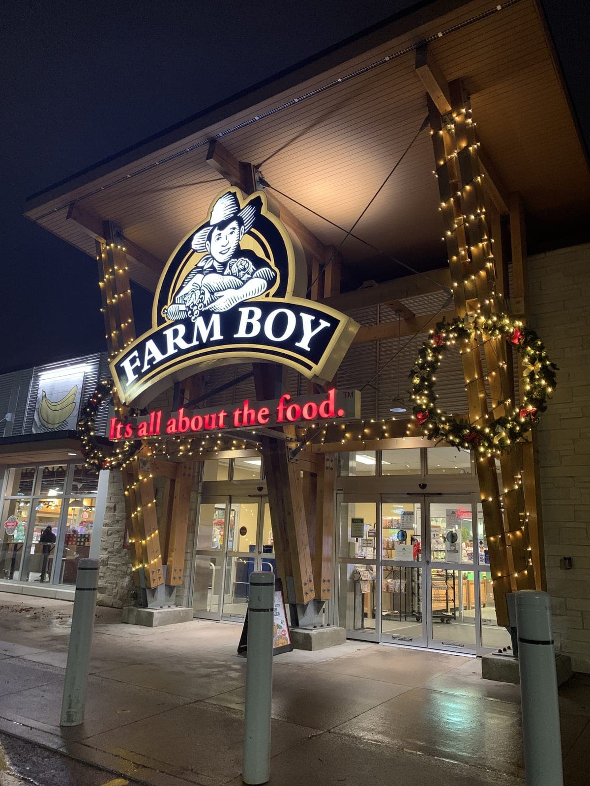 Grocery store entrance framed with warm-white Christmas lights and a lit holiday wreath at night