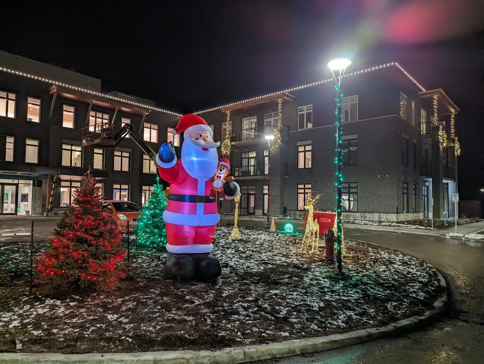Large illuminated inflatable Santa and lit Christmas trees at a commercial property decorated with roofline lights