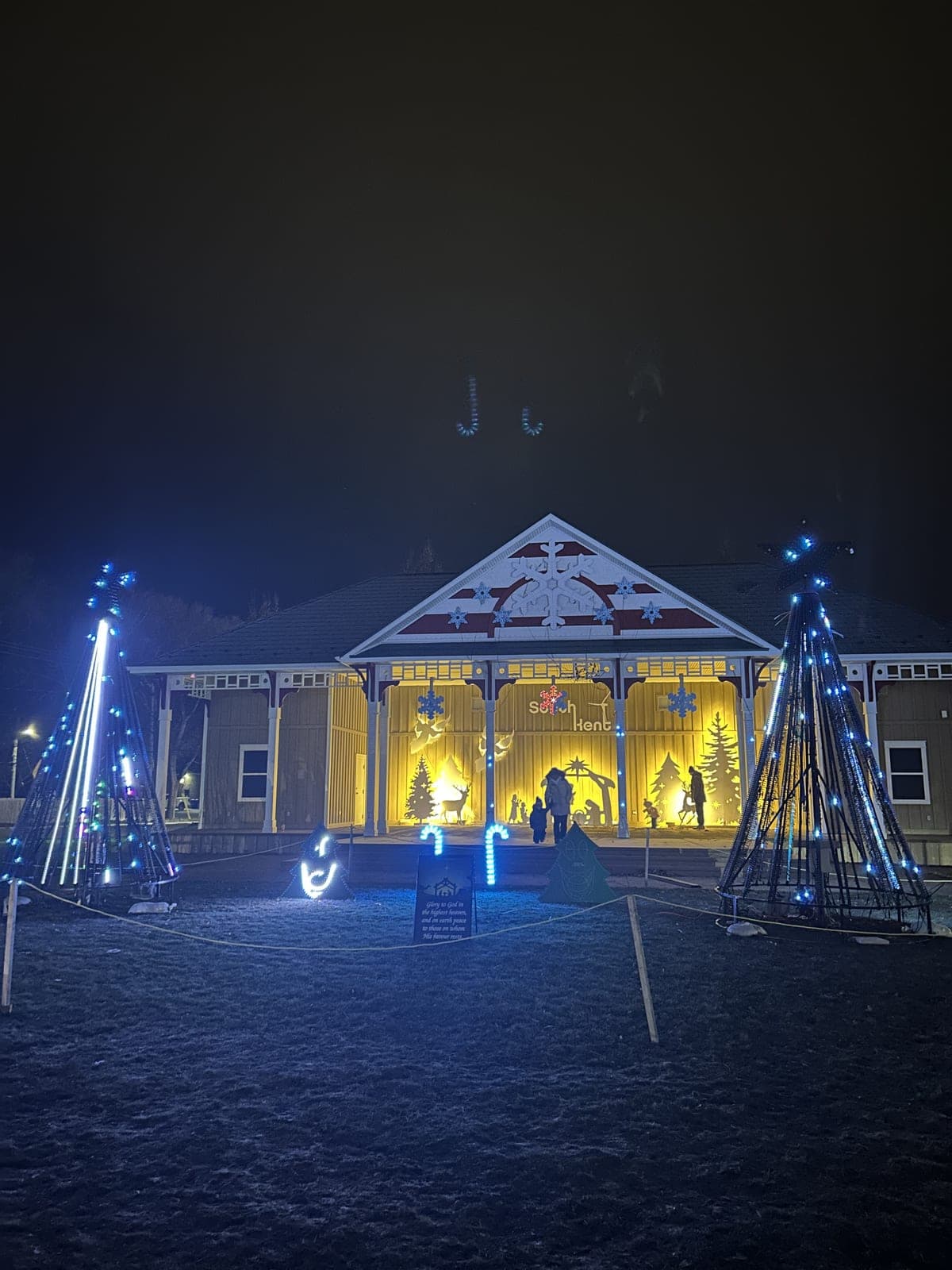 Outdoor community holiday light display with an illuminated pavilion, blue snowflake lights and glowing silhouette scenes at night