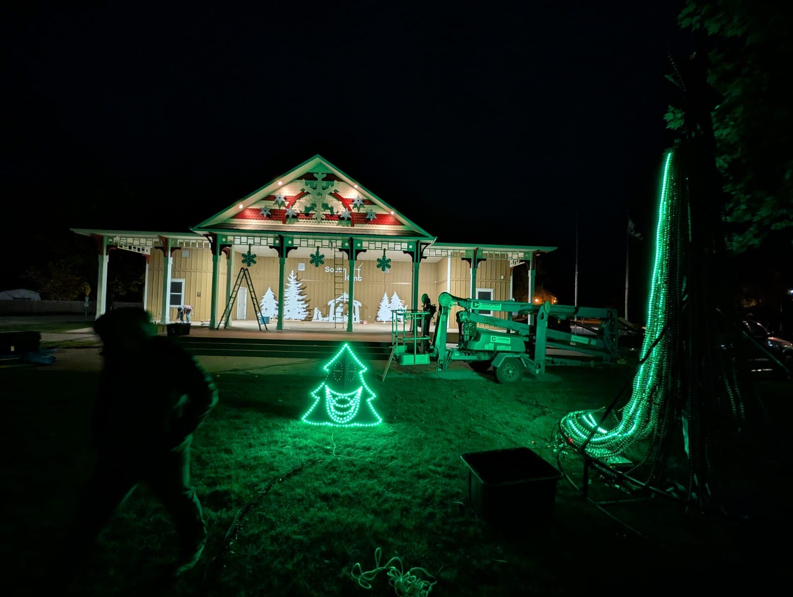 Crew installing Christmas lights and LED displays at a park pavilion at night.