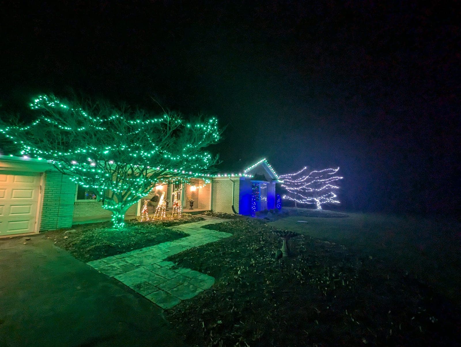 Ranch home with a green-wrapped front tree and warm-white roofline Christmas lights
