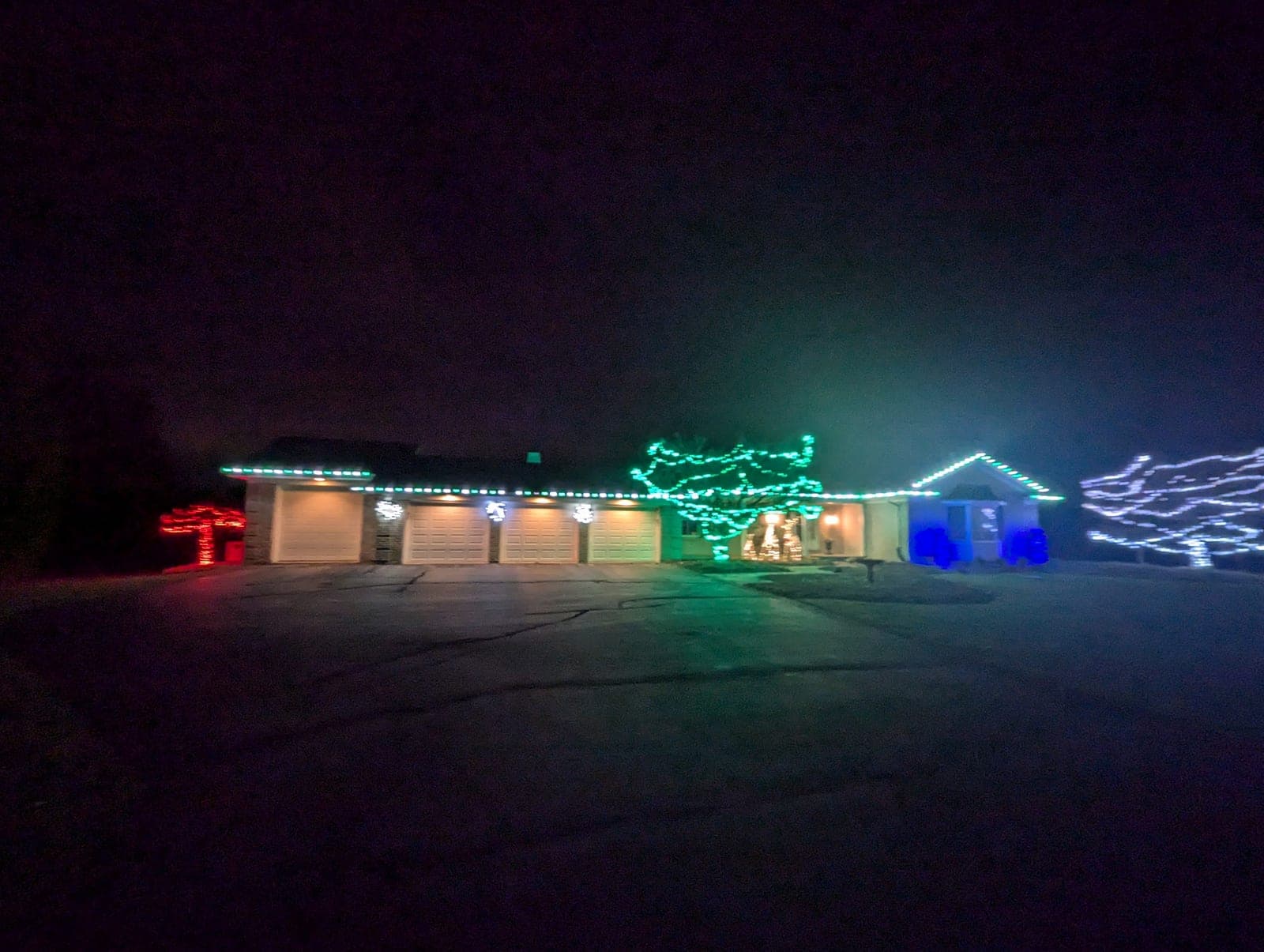 Wide view of a ranch home decorated with multicolour Christmas lights and lit yard trees