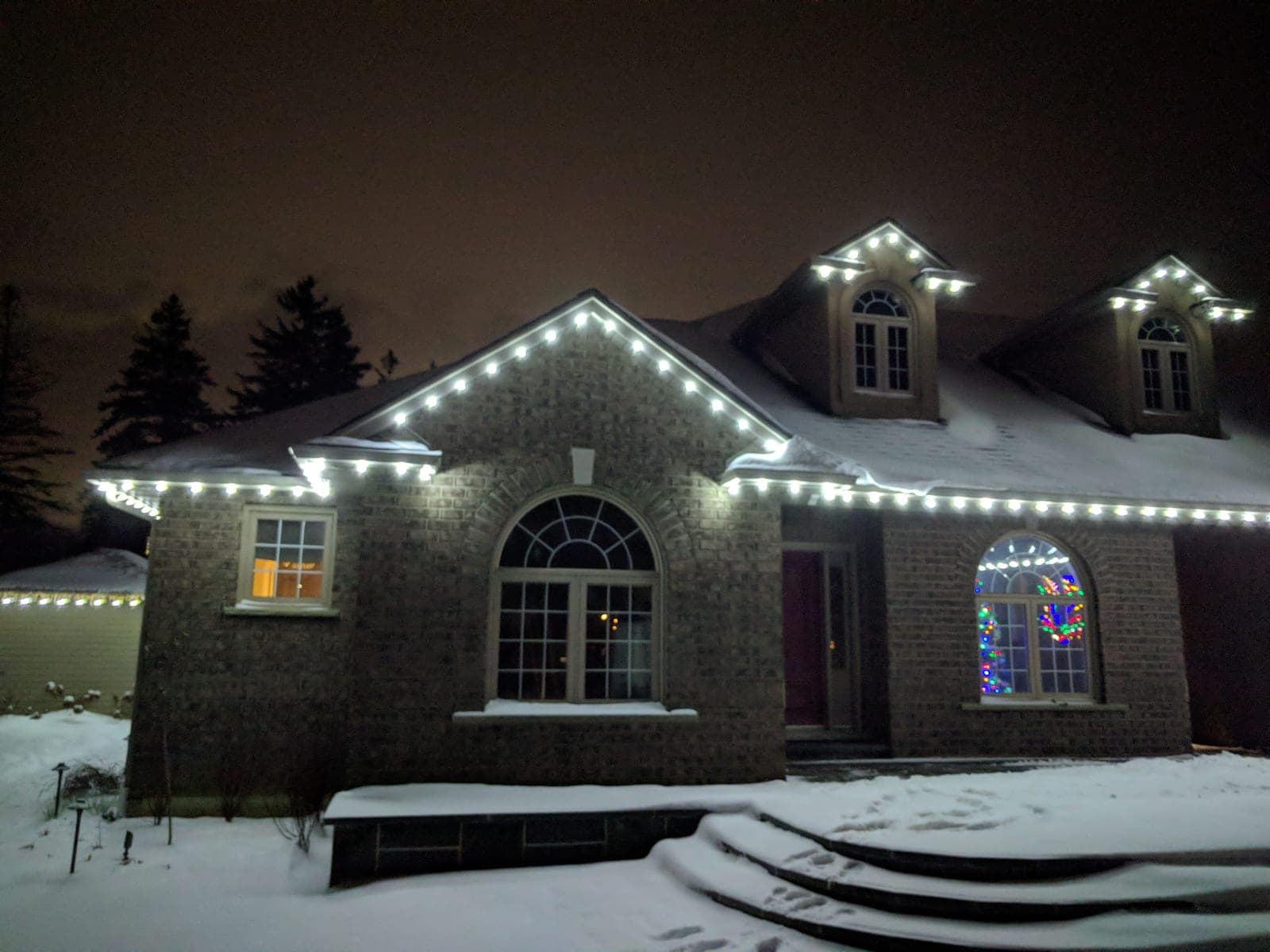 Two-storey brick home outlined in white Christmas roofline lights with snow-covered front steps