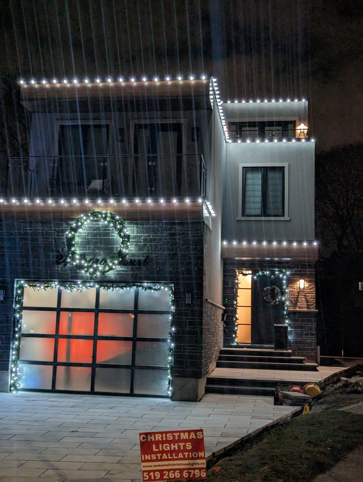 Two-storey home with warm-white roofline Christmas lights and lit garland at the front entrance