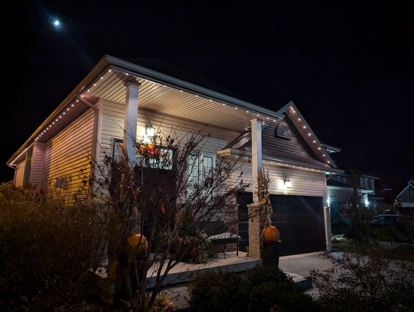 Two-storey home lined with warm-white roofline Christmas lights under a bright moon