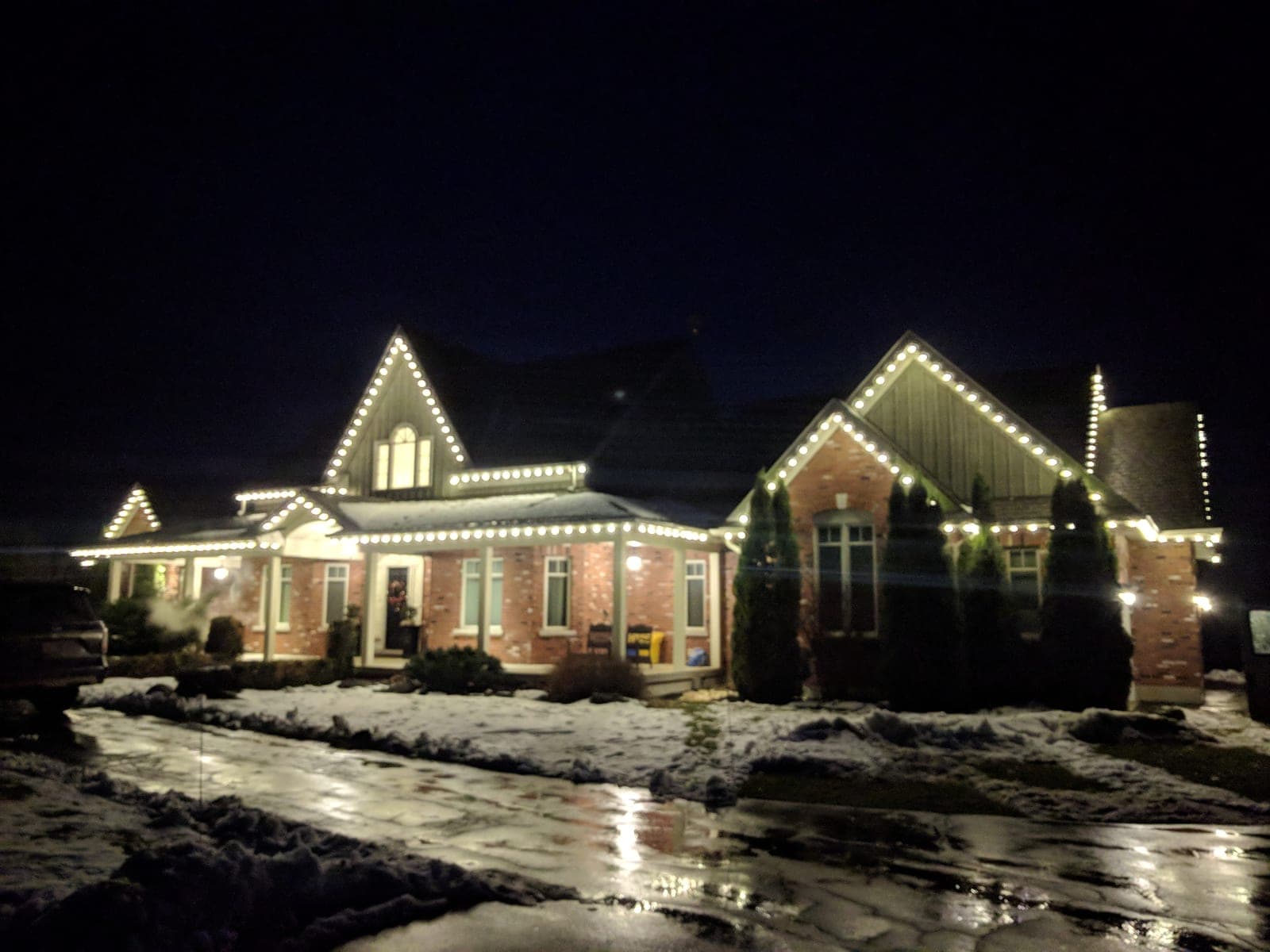 Warm-white C9 roofline lights outlining the gables of a large brick country home at night.