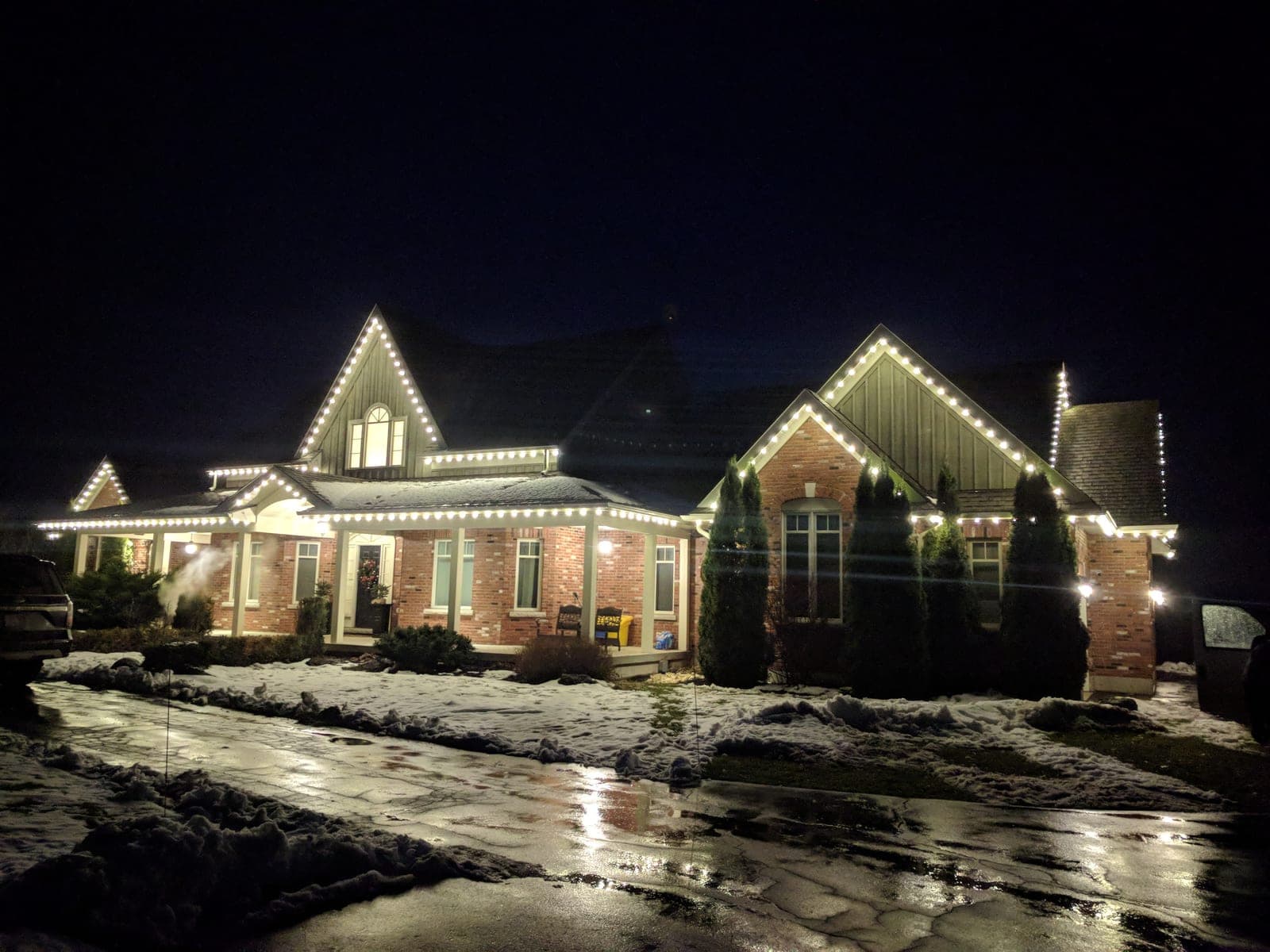 Wide view of a brick country home outlined in warm-white C9 roofline Christmas lights.