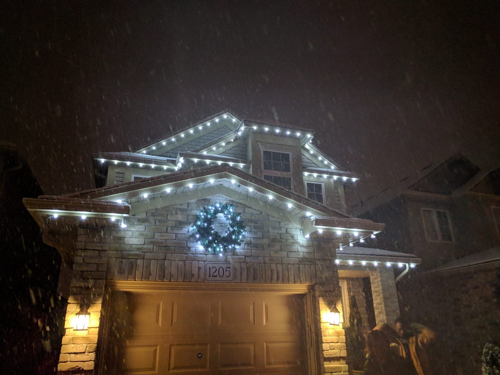 Warm white C9 roofline Christmas lights outlining a two-storey brick home during evening snowfall.