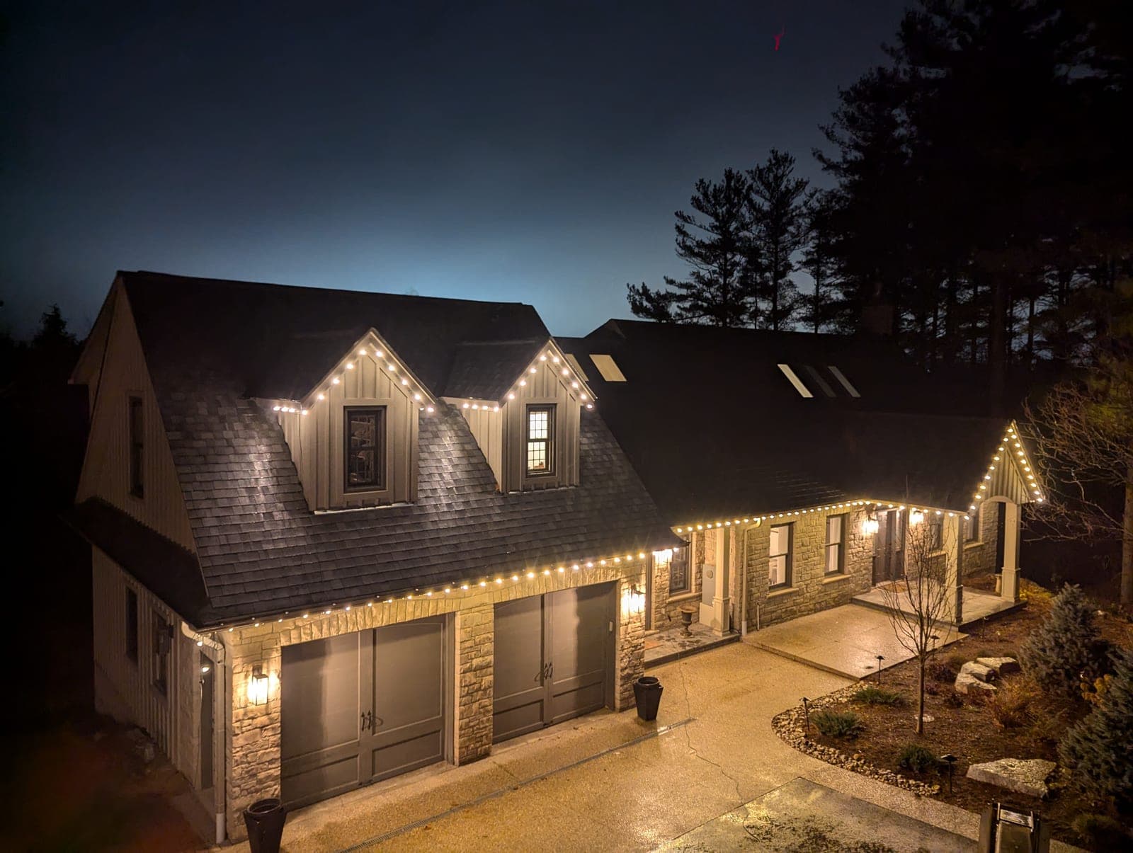 Warm-white roofline Christmas lights tracing a two-storey home and stone garage at night